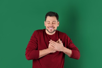 Portrait of handsome man holding hands near his heart on color background