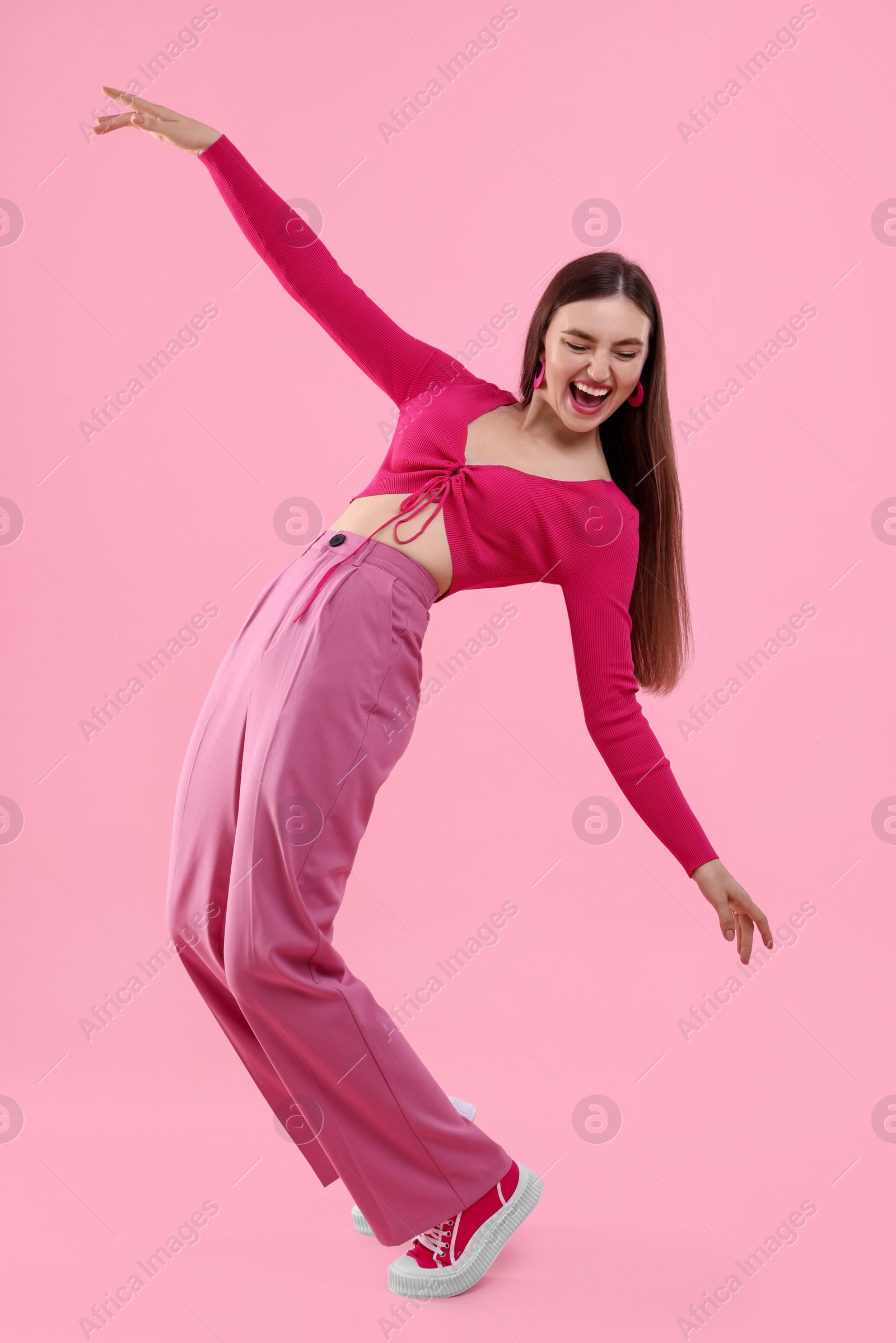 Photo of Beautiful young woman in pink clothes dancing on color background