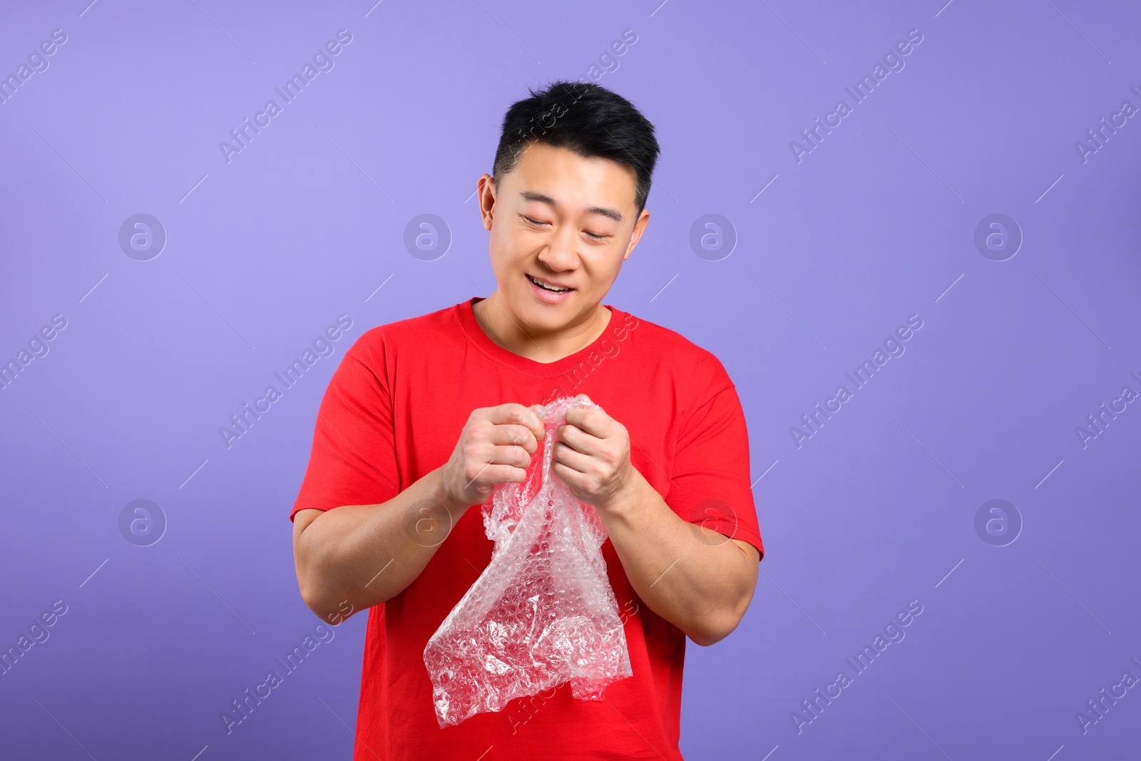 Photo of Happy asian man with bubble wrap on purple background