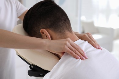 Photo of Man receiving massage in modern chair indoors, closeup