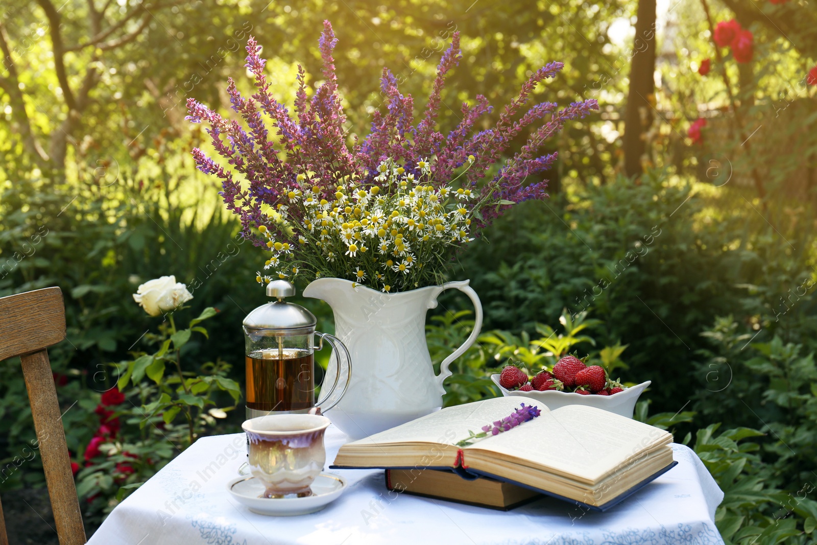 Photo of Beautiful bouquet of wildflowers and books on table served for tea drinking in garden