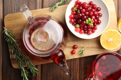 Photo of Tasty hot cranberry tea, lemon, rosemary and fresh berries on wooden table