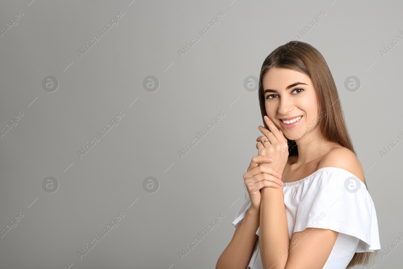 Photo of Happy young woman wearing beautiful engagement ring on grey background