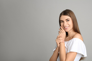 Happy young woman wearing beautiful engagement ring on grey background