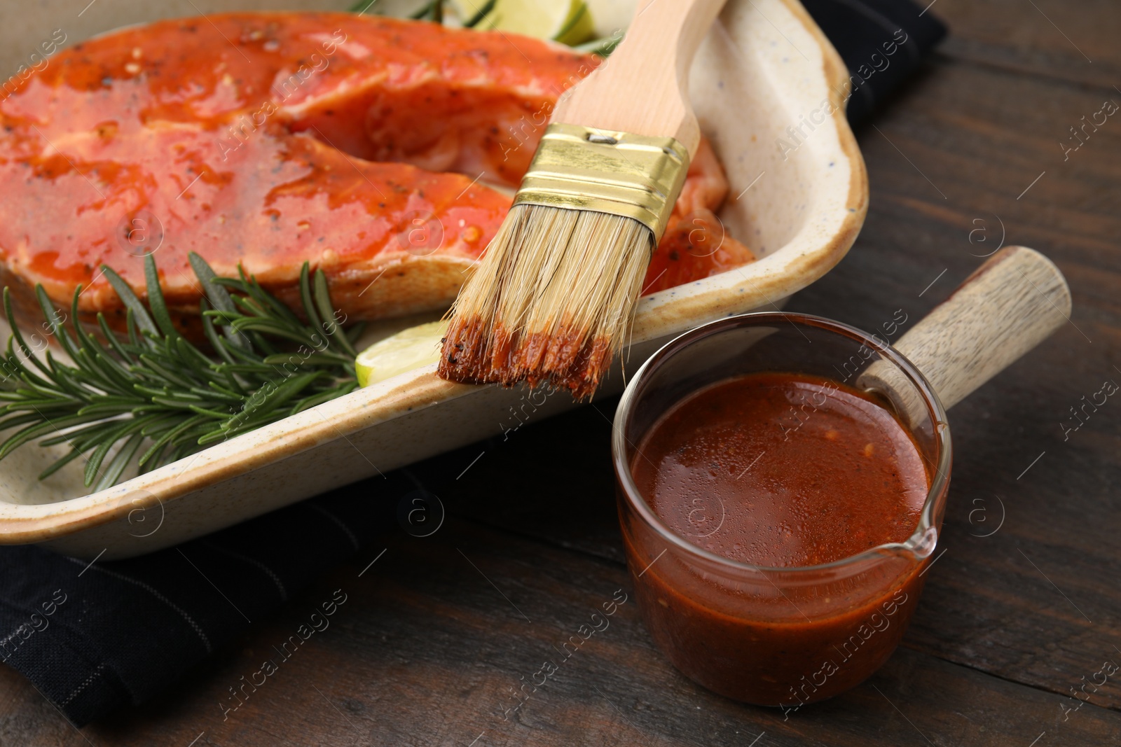 Photo of Fresh marinade, fish, rosemary, lime and brush on wooden table, closeup