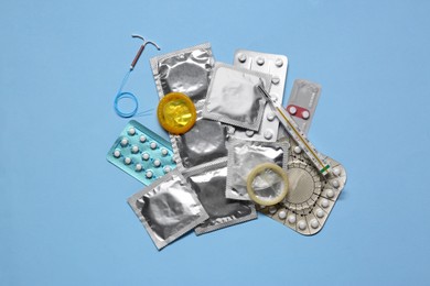 Photo of Contraceptive pills, condoms, intrauterine device and thermometer on light blue background, flat lay. Different birth control methods
