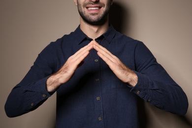 Photo of Man showing HOUSE gesture in sign language on color background, closeup