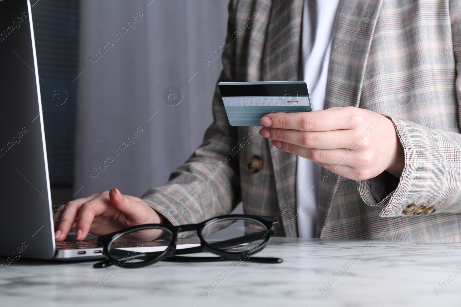 Photo of Online payment. Woman with laptop and credit card at white marble table, closeup