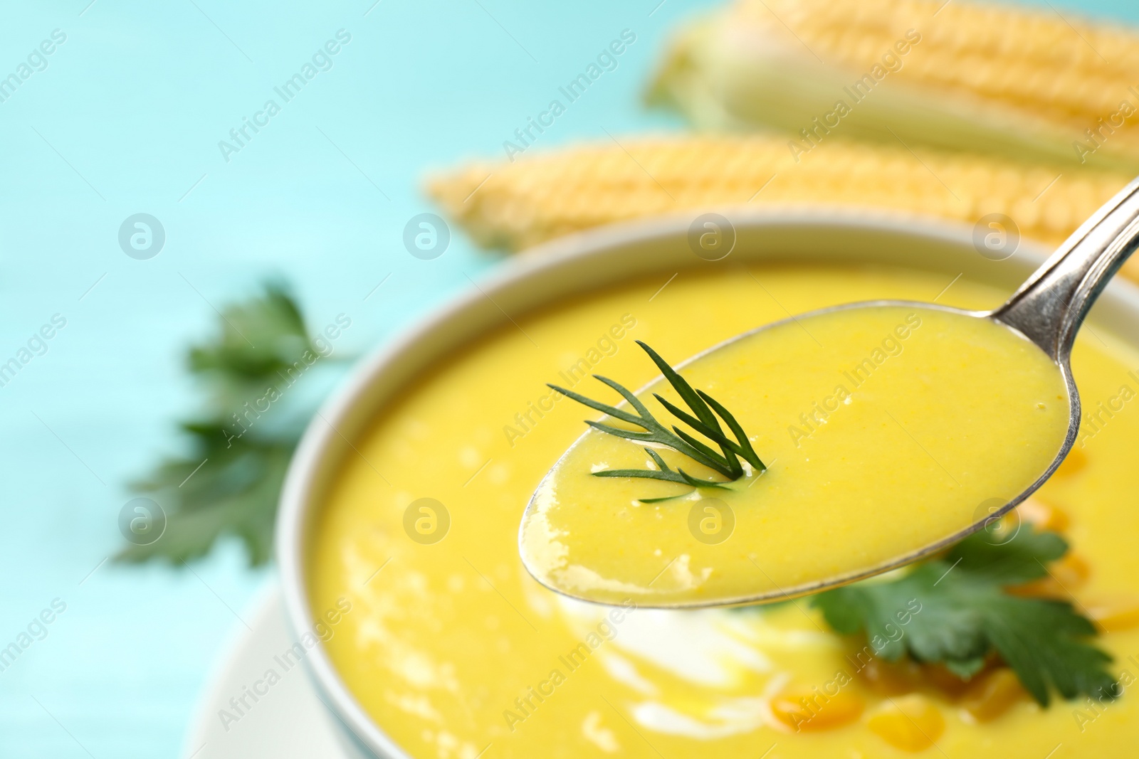 Photo of Spoon of delicious corn soup over full bowl, closeup