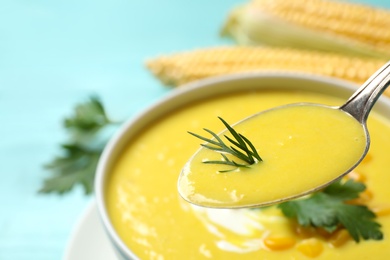 Photo of Spoon of delicious corn soup over full bowl, closeup