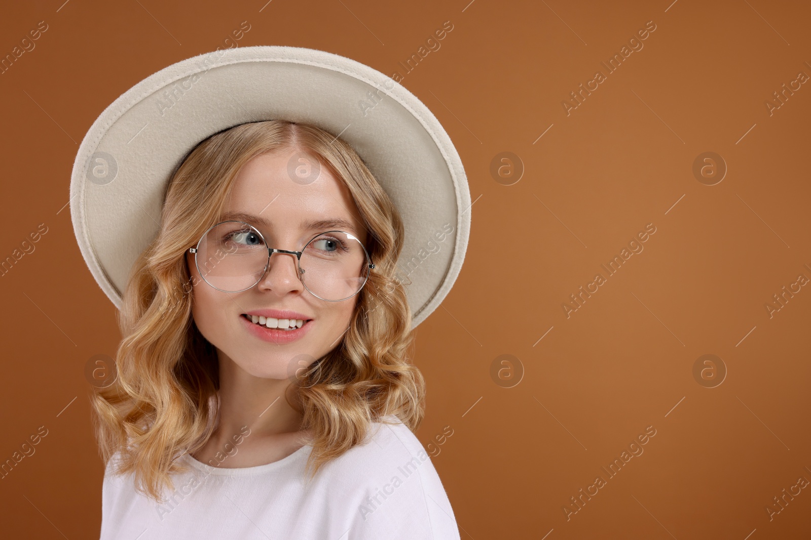Photo of Beautiful woman with blonde hair in hat on brown background. Space for text