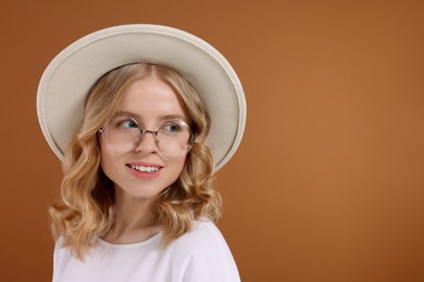 Photo of Beautiful woman with blonde hair in hat on brown background. Space for text