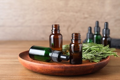 Photo of Plate with bottles of essential oils and rosemary on wooden table