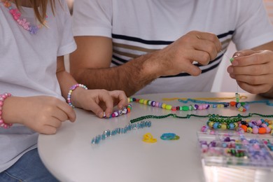 Photo of Father with his daughter making beaded jewelry at table, closeup