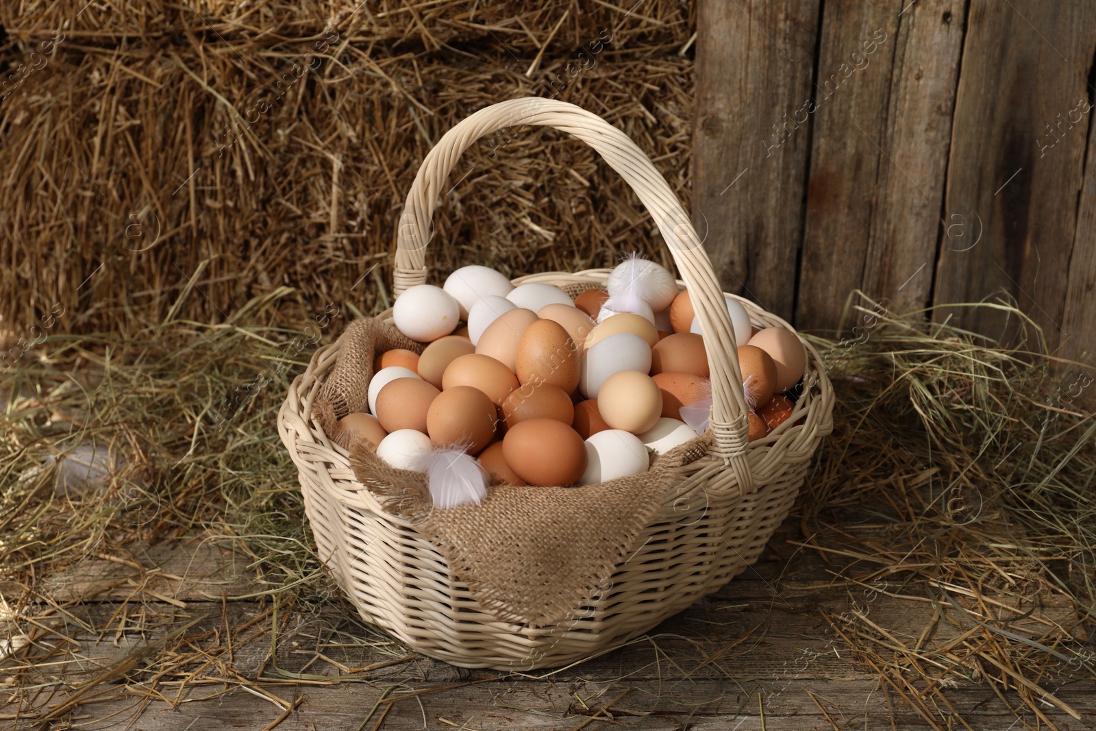 Photo of Wicker basket with fresh chicken eggs and dried straw in henhouse