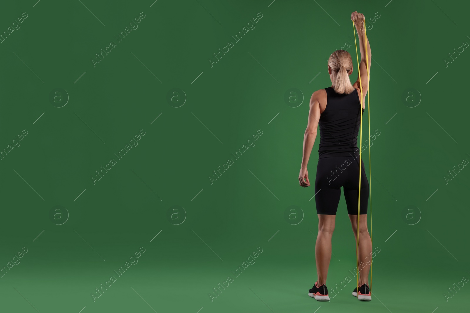 Photo of Athletic woman exercising with elastic resistance band on green background, back view. Space for text