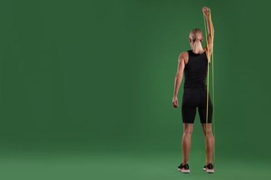 Photo of Athletic woman exercising with elastic resistance band on green background, back view. Space for text