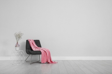 Photo of Stylish room interior with comfortable chair and plaid near white wall. Space for text