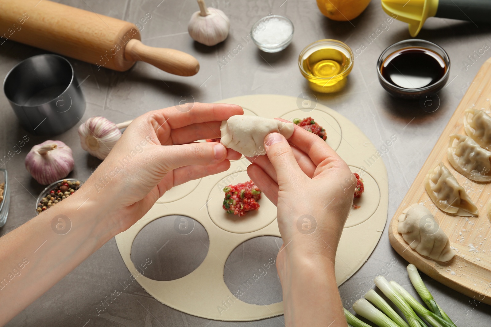 Photo of Woman cooking delicious gyoza at light grey table, closeup