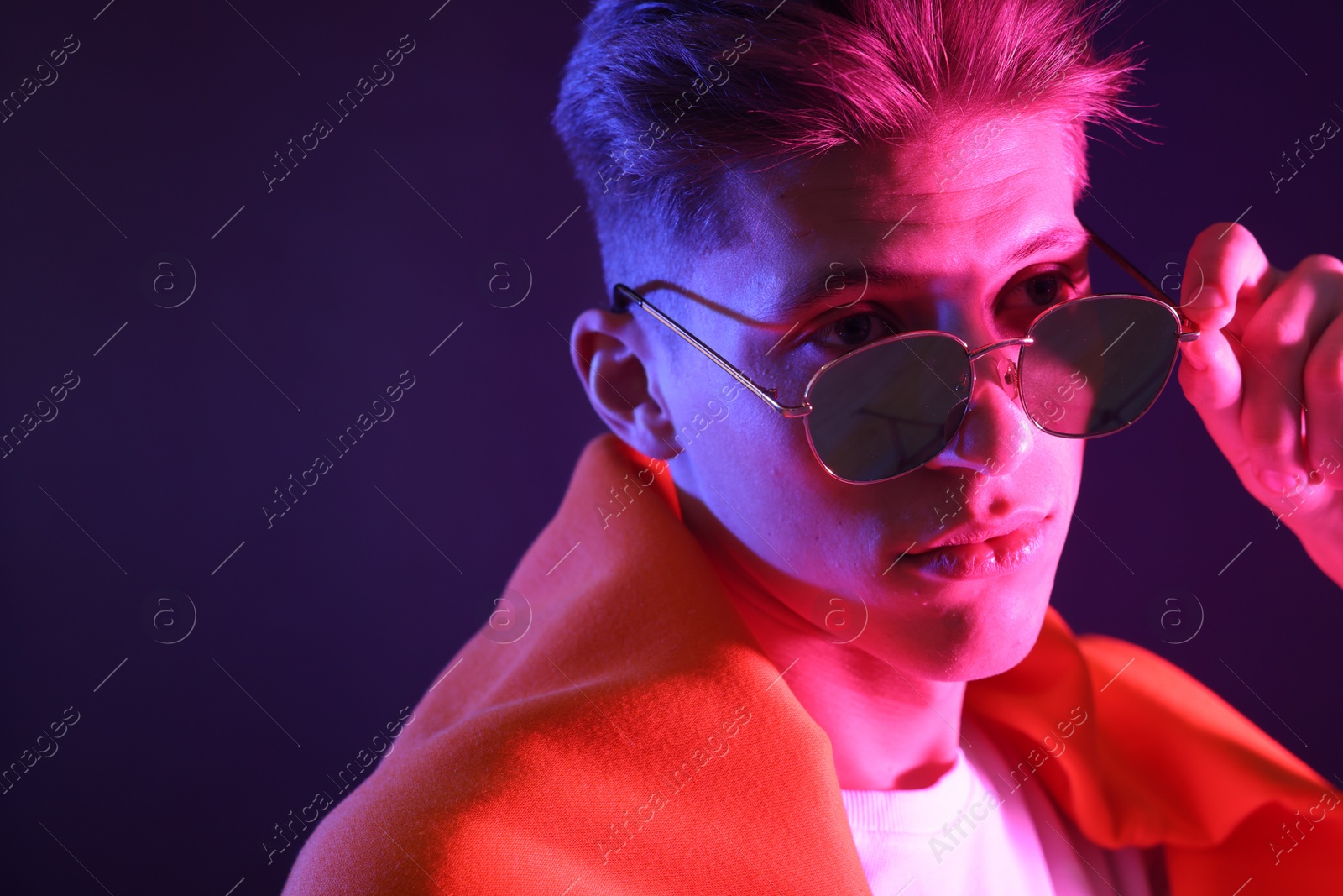 Photo of Stylish young man in sunglasses on dark background in neon lights