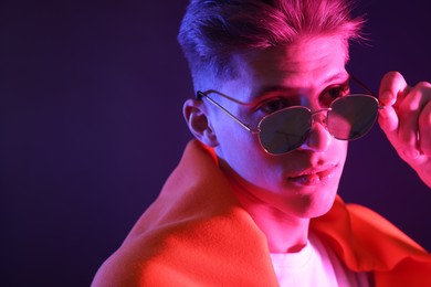 Photo of Stylish young man in sunglasses on dark background in neon lights