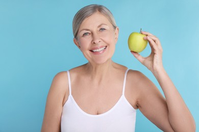 Beautiful woman with fresh apple on light blue background. Vitamin rich food