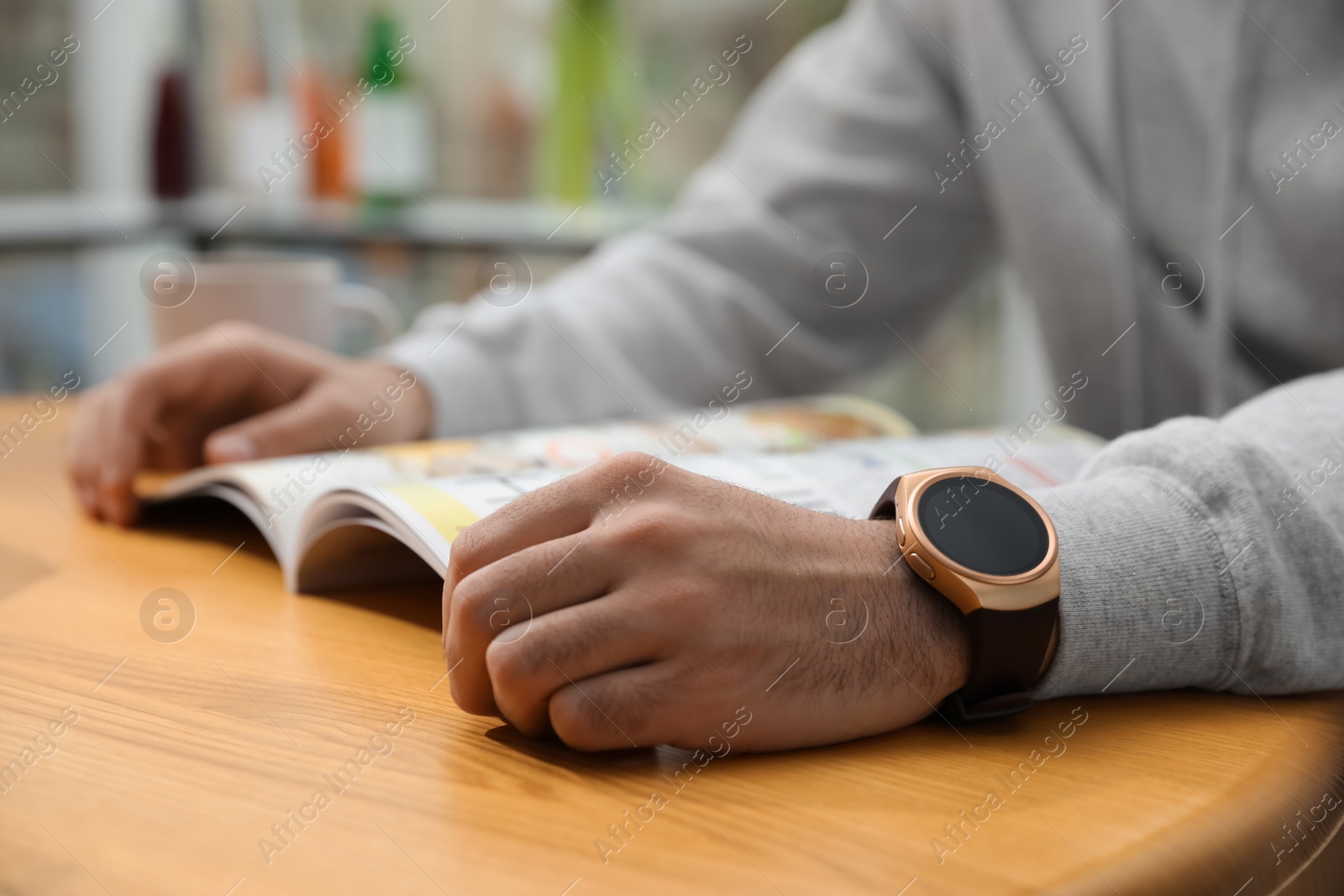 Photo of Man wearing smart watch and reading magazine at table indoors, closeup