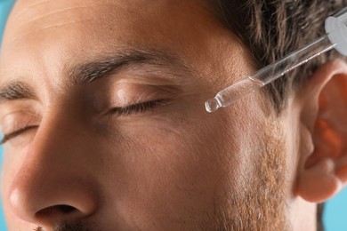 Photo of Handsome man applying cosmetic serum onto his face, closeup