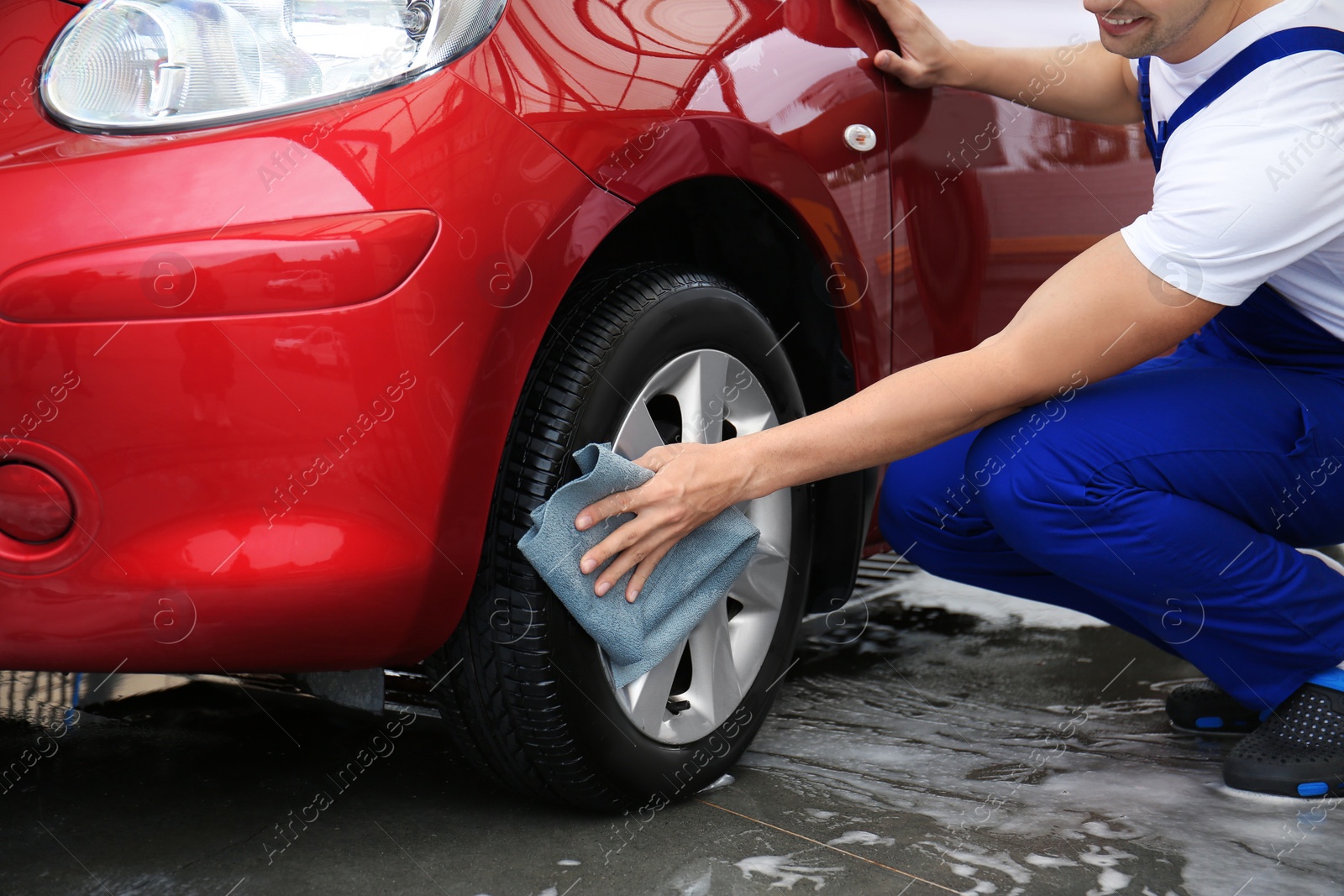 Photo of Male worker cleaning vehicle wheel with cloth at car wash