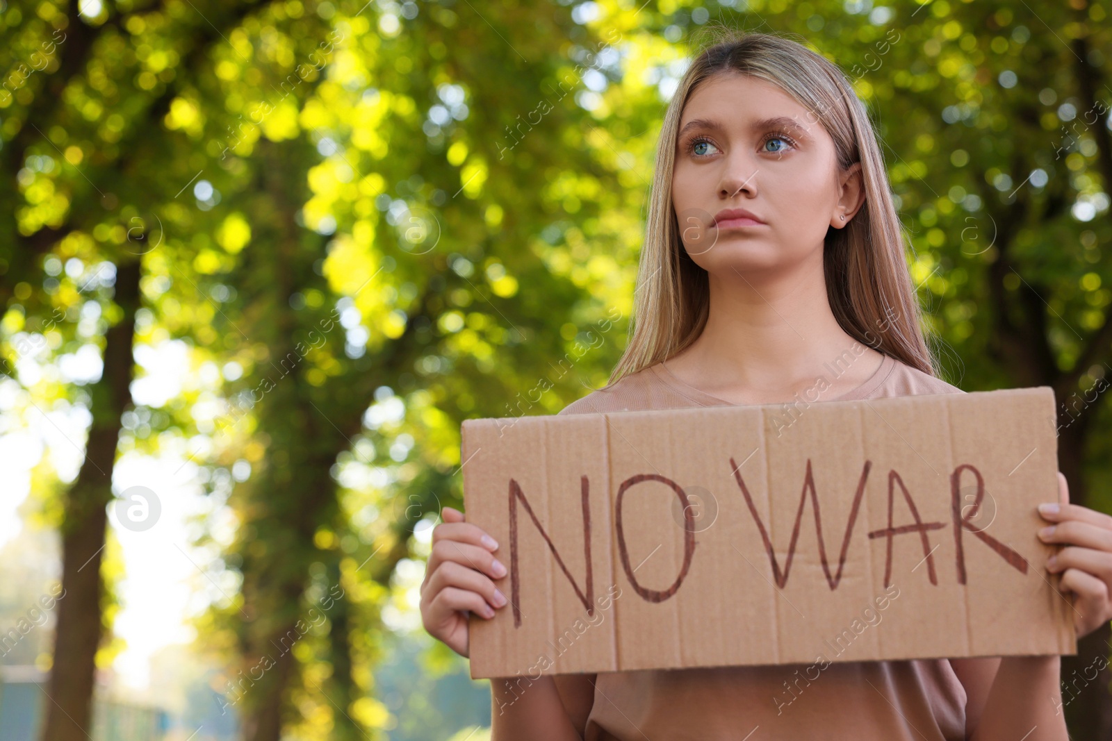 Photo of Sad woman holding poster with words No War in park. Space for text