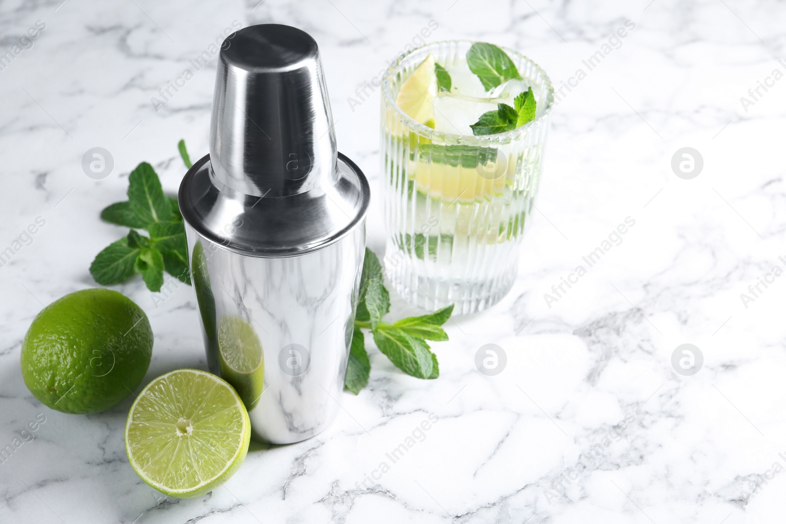 Photo of Metal cocktail shaker, delicious mojito, limes and mint on white marble table, space for text