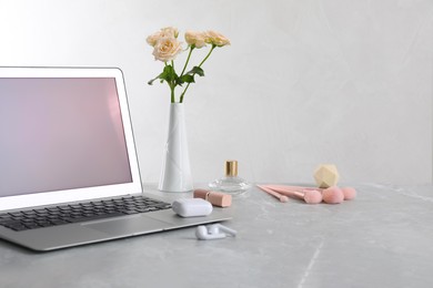 Photo of Modern laptop, flowers and makeup products on grey marble table. Space for design
