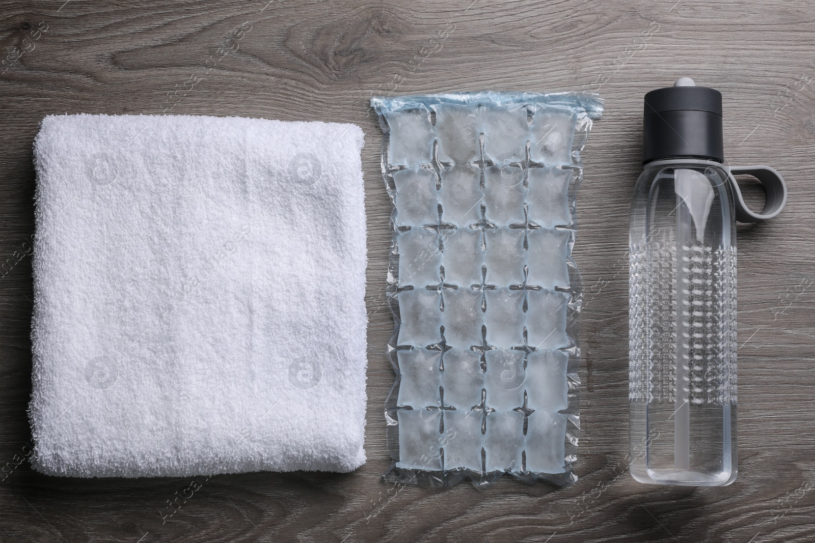 Photo of Bottle of water, ice pack and towel on wooden background, flat lay. Heat stroke treatment