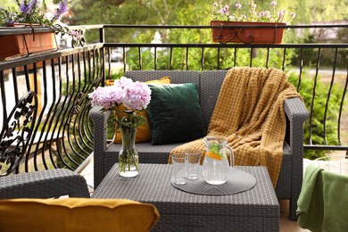 Photo of Rattan table with jug of water, glasses and beautiful flowers on terrace