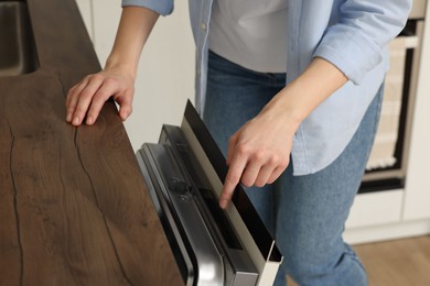 Woman pushing button on dishwasher's door indoors, closeup