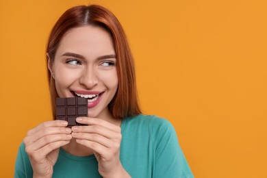 Young woman eating tasty chocolate on orange background, space for text