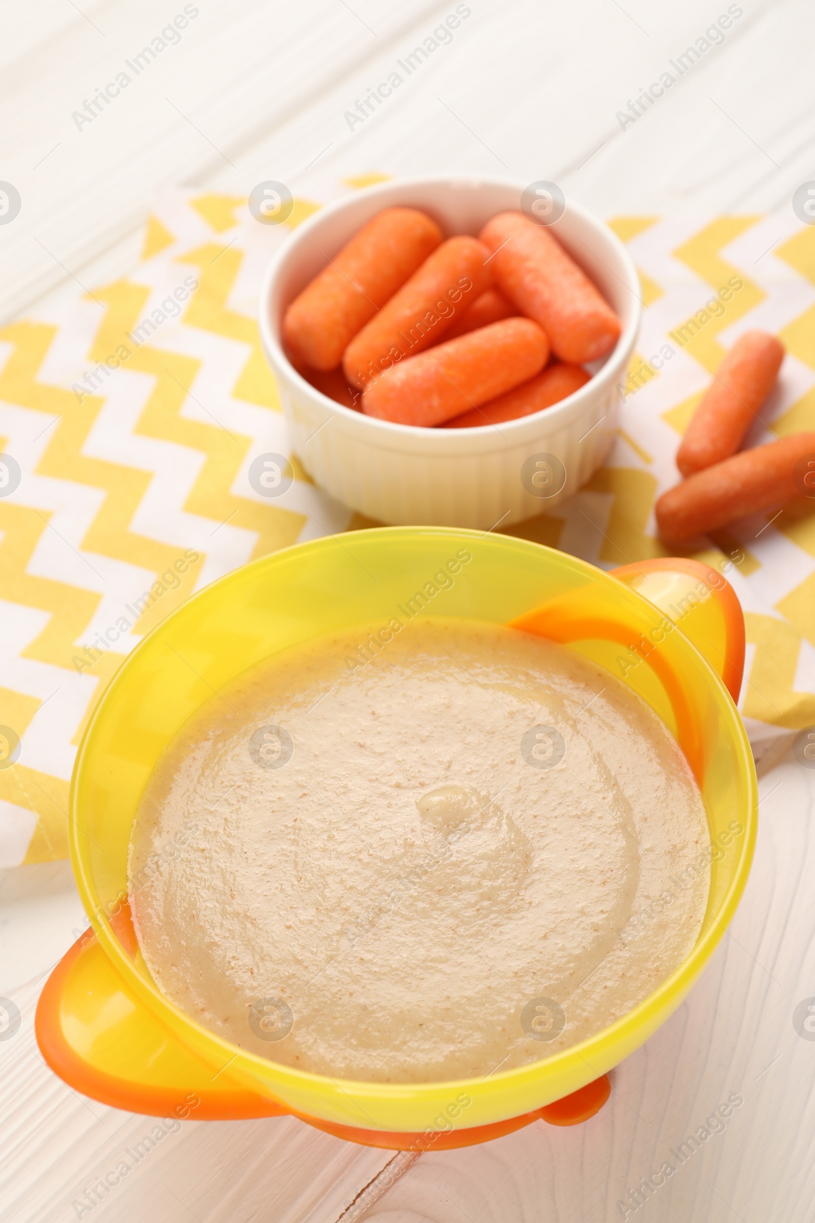 Photo of Baby food. Puree in bowl and small carrots on white wooden table