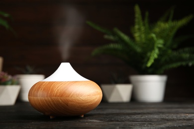 Composition with modern essential oil diffuser on black wooden table against dark background, space for text