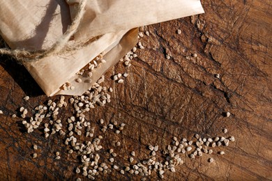 Paper bag with scattered tomato seeds on wooden background, top view and space for text. Vegetable planting