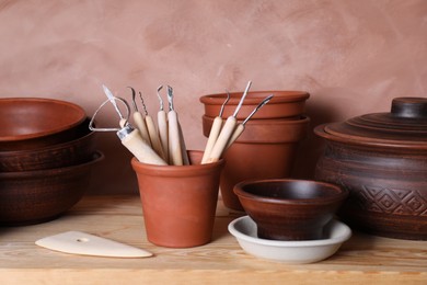 Set of different crafting tools and clay dishes on wooden table in workshop