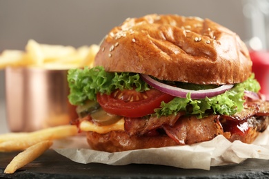 Photo of Delicious burger with bacon and french fries on slate plate