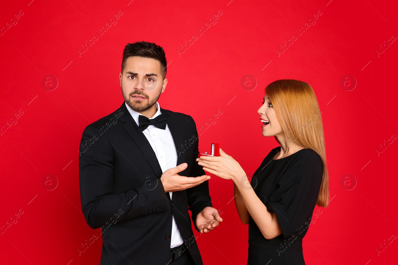 Photo of Young woman with engagement ring making marriage proposal to her boyfriend on red background