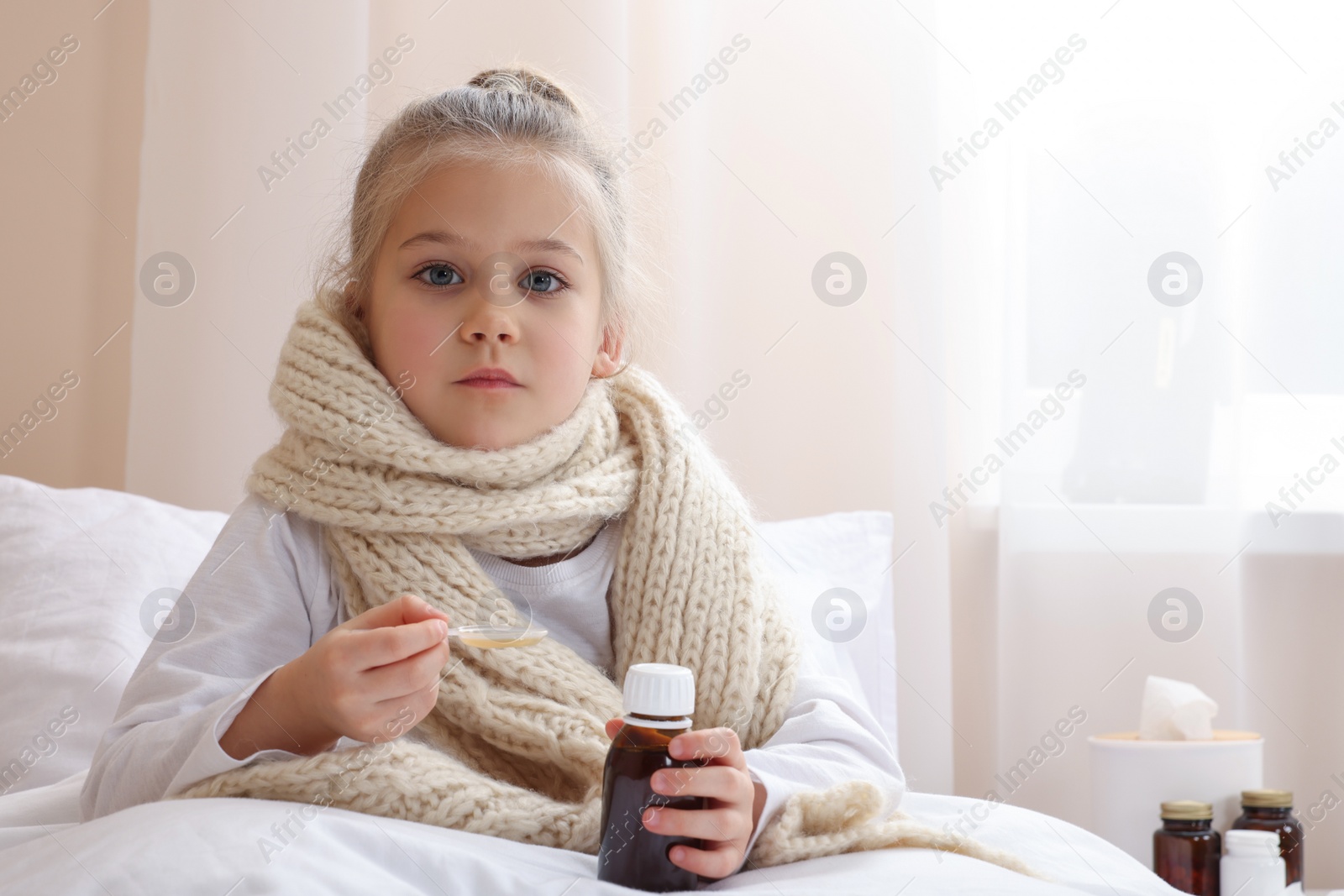 Photo of Sick girl taking cough syrup on bed at home, space for text. Cold medicine