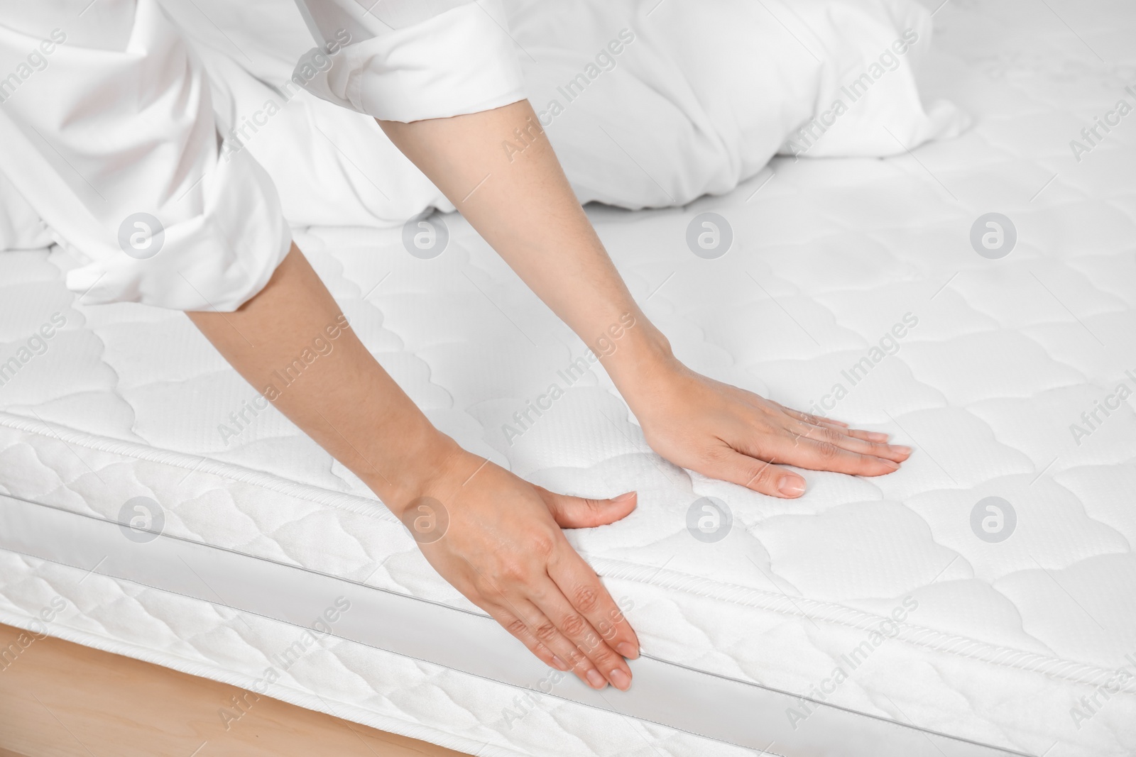 Photo of Woman touching soft white mattress on bed, closeup