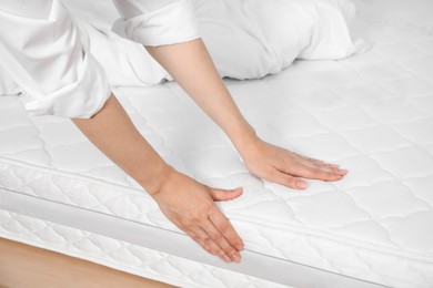 Woman touching soft white mattress on bed, closeup