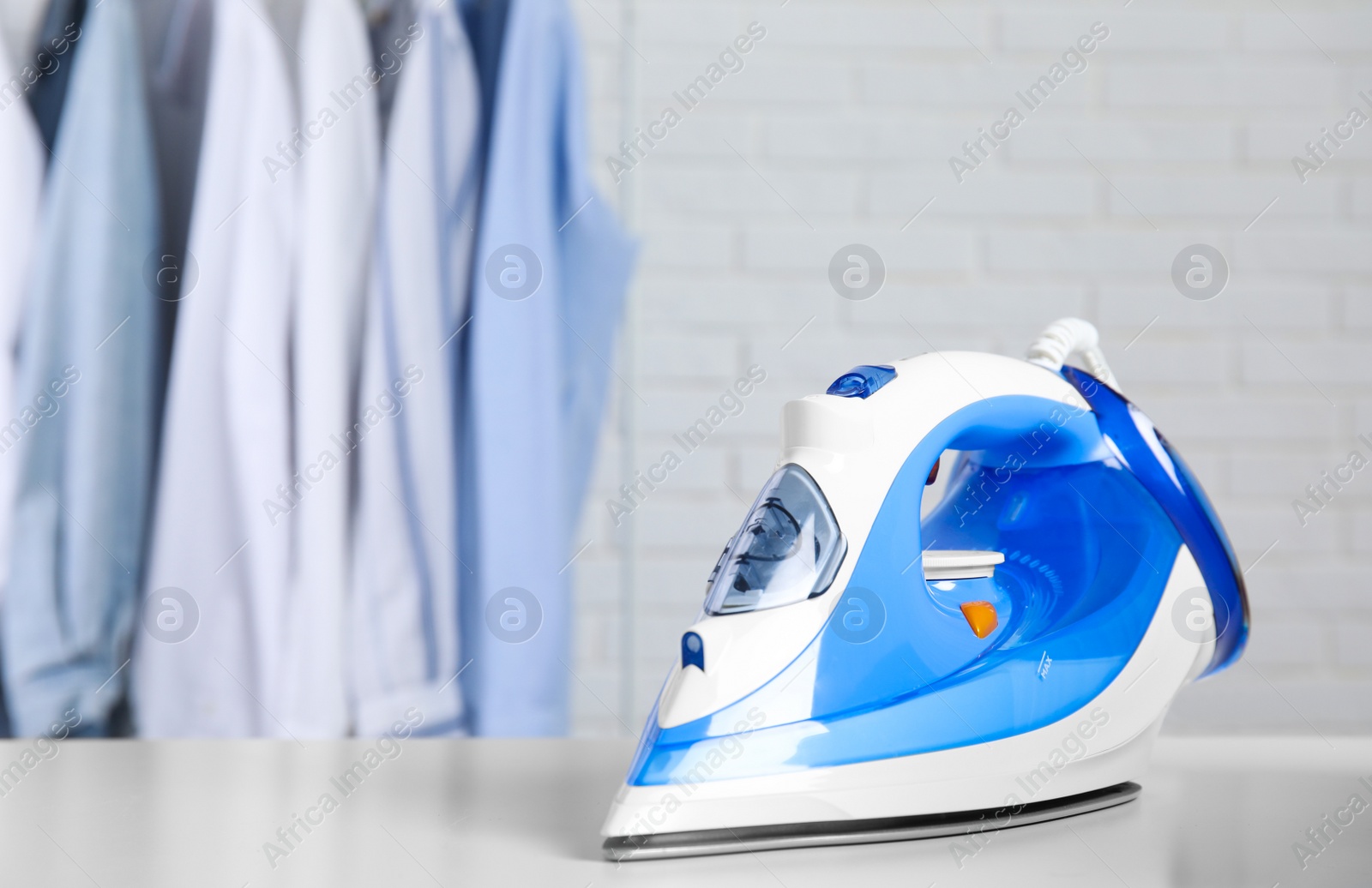 Photo of Modern iron on table near rack with clean clothes indoors, space for text