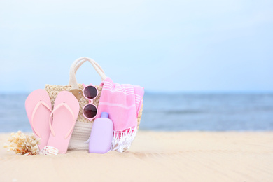 Bag with beach objects on sand near sea, space for text