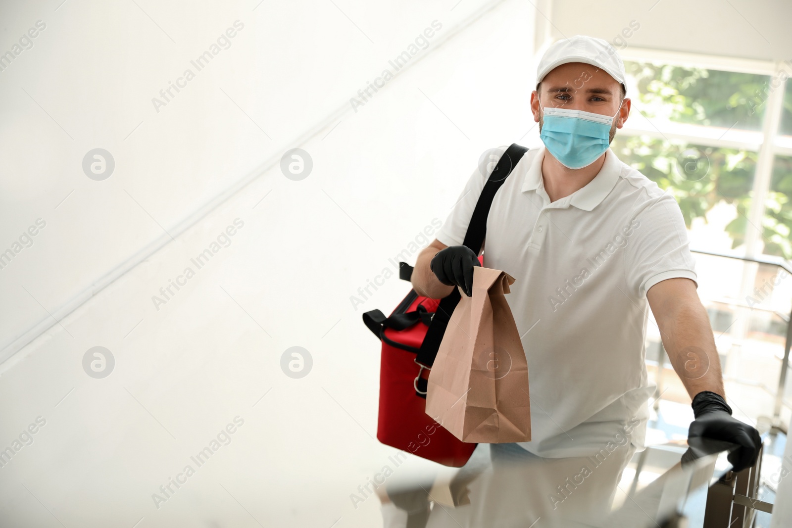 Photo of Courier in protective mask and gloves with order indoors. Restaurant delivery service during coronavirus quarantine