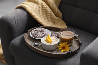 Wooden tray with delicious breakfast and beautiful flower on armchair indoors