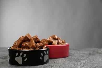 Photo of Wet pet food in feeding bowls on grey table. Space for text